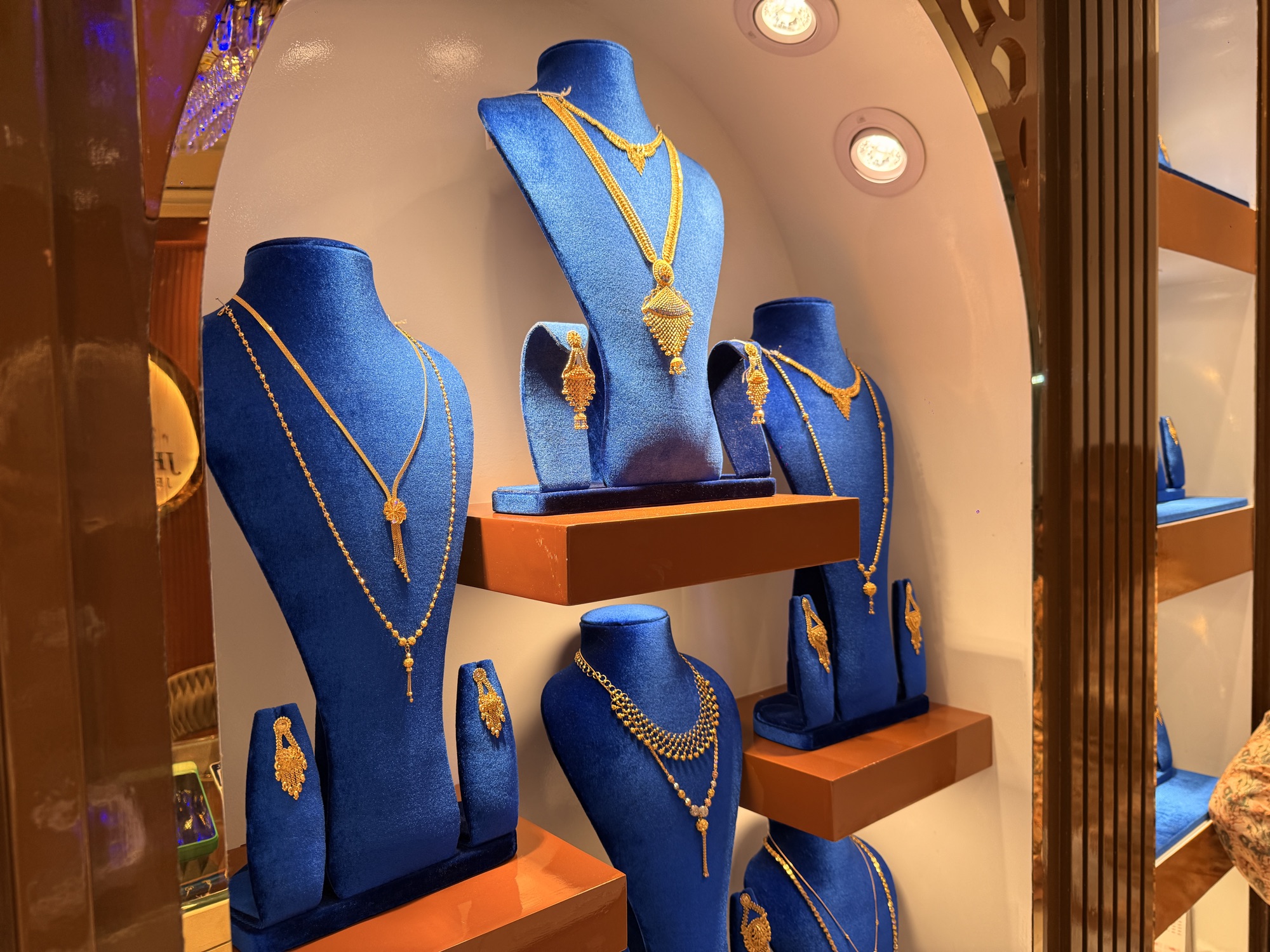 Wide view of gold necklace sets displayed in a carved blue and gilt alcove.