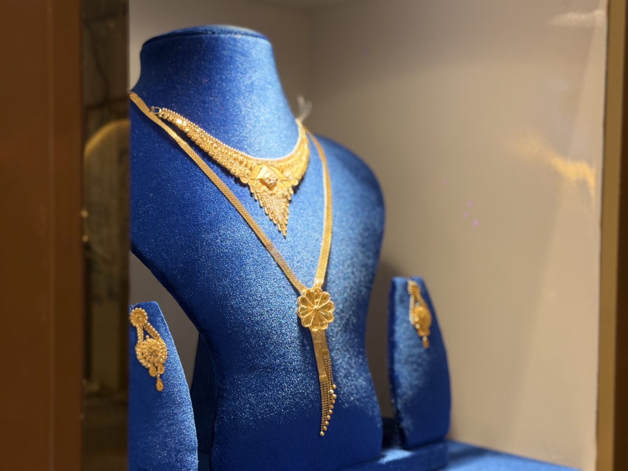 Side view of a layered yellow gold necklace and floral pendant on a blue velvet display.